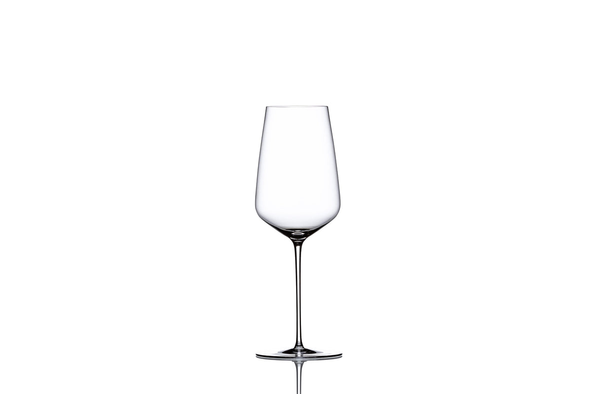 Ritual white wine in a clear glass bottle with a white label, served in a wine glass, on a wooden table background.