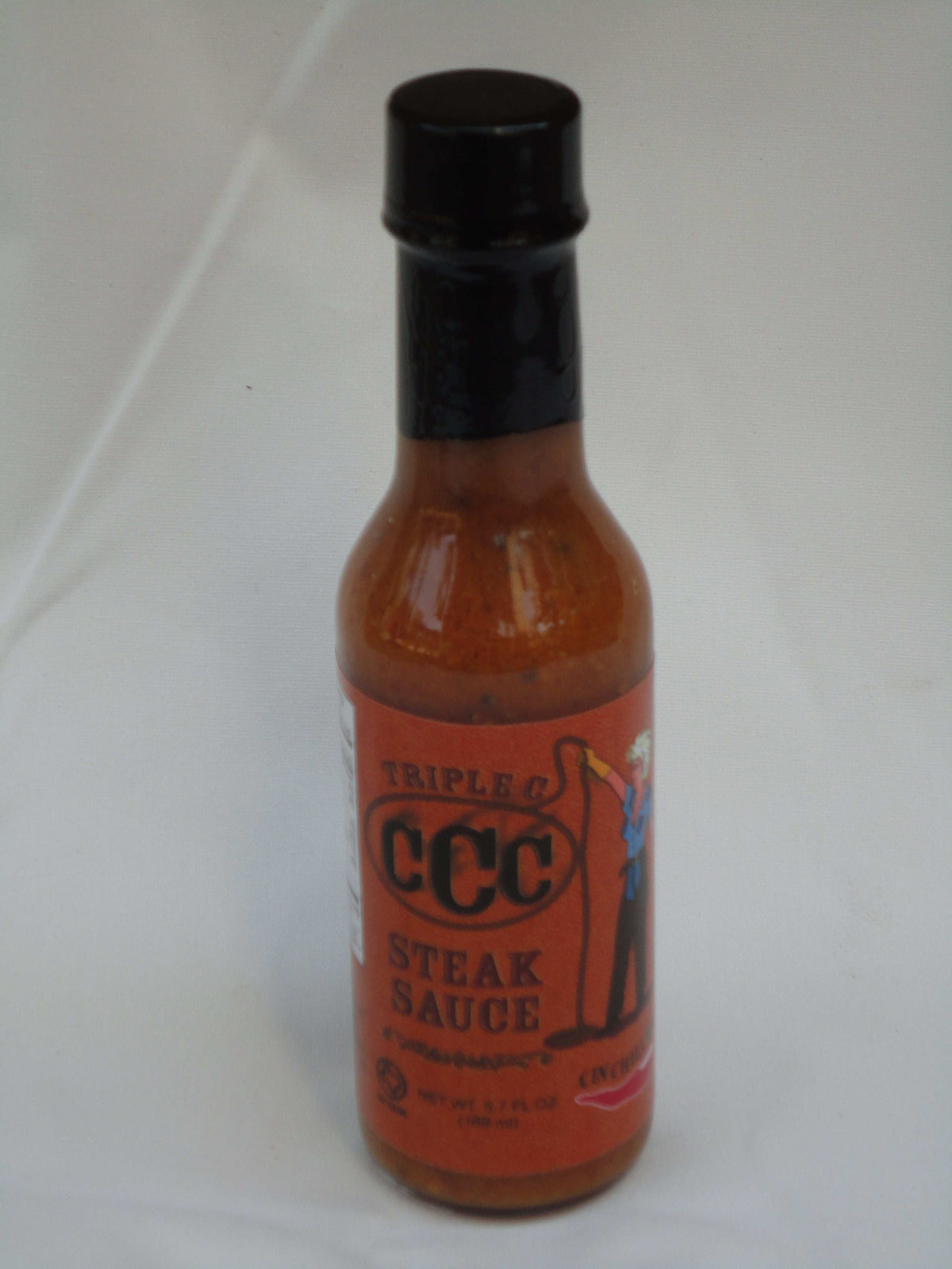 Cinderosa Ranch Triple C Steak Sauce hot sauce bottle with a red label and metal cap, placed on a wooden surface.