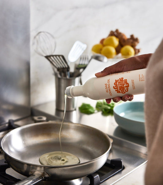 Bottle of Algae Cooking Club algae cooking oil with a clear label, shown in a kitchen setting on a countertop.