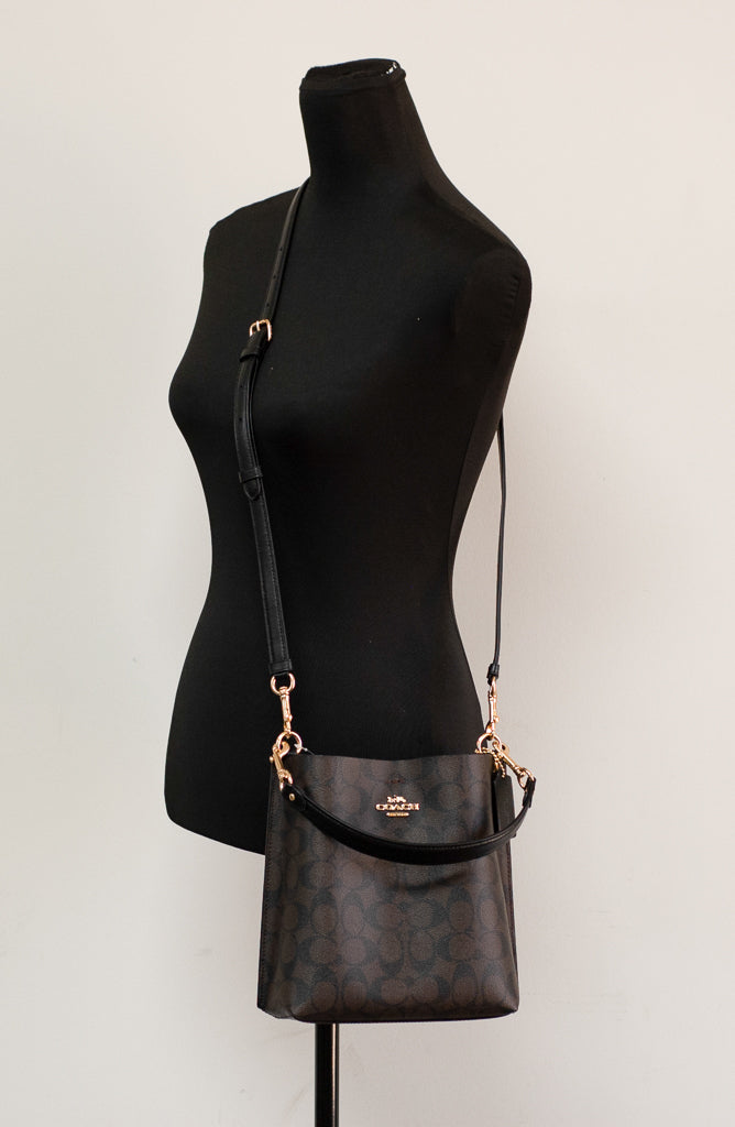 Coach Mollie 22 small bucket crossbody handbag in brown and black coated canvas with adjustable strap and signature design.