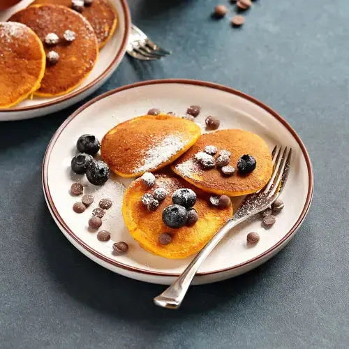 Plate of chocolate chip pancakes by AmBari Nutrition, topped with syrup and fresh berries, served on a white plate.
