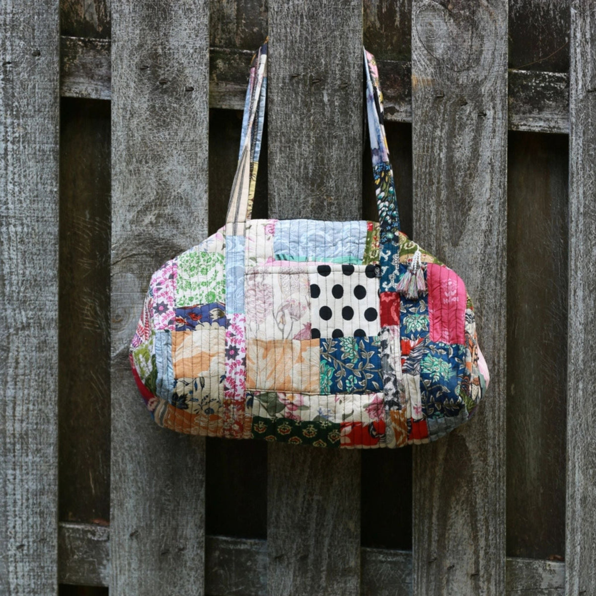 Patchwork quilted duffle bag from Darn Good Yarn with colorful fabric patches and sturdy handles.