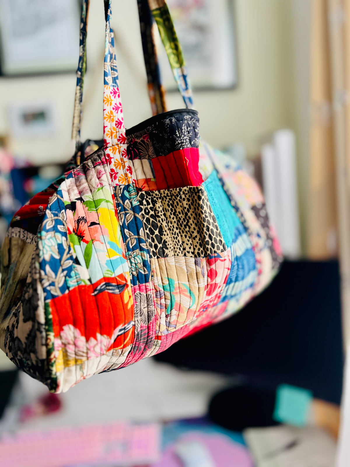 Colorful patchwork quilted duffle bag with Darn Good Yarn branding, showcasing its spacious design and textured fabric.