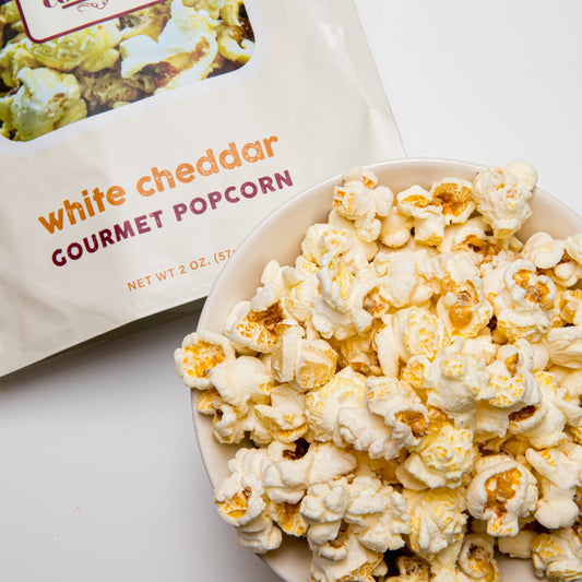 White cheddar popcorn from Colorado Popcorn Company in a 2 oz bag, showing crispy, cheesy popcorn pieces on a white background.