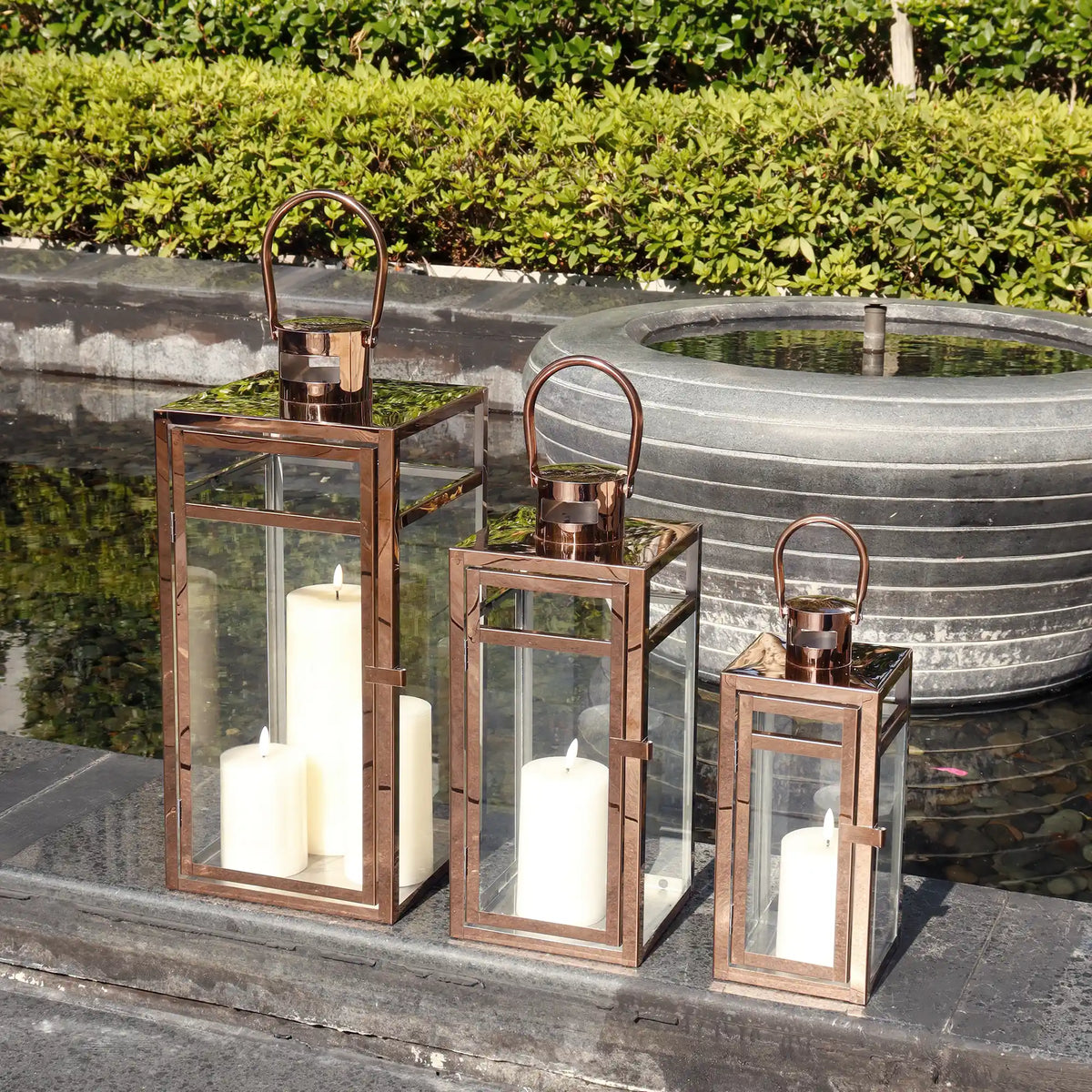Set of three rose gold stainless steel decorative candle lanterns in 12, 15, and 19-inch sizes with hurricane-style design.