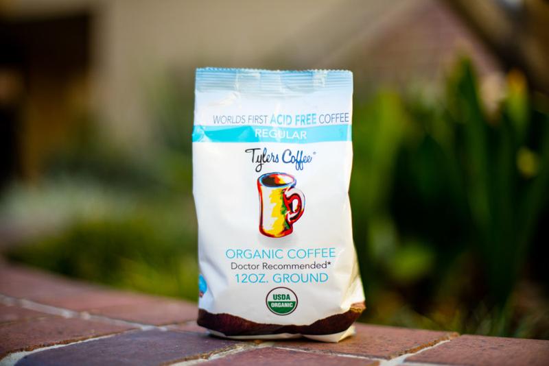 Bag of Tylers Coffees regular acid-free ground coffee with a rustic label and a scoop of coffee grounds on a wooden surface.