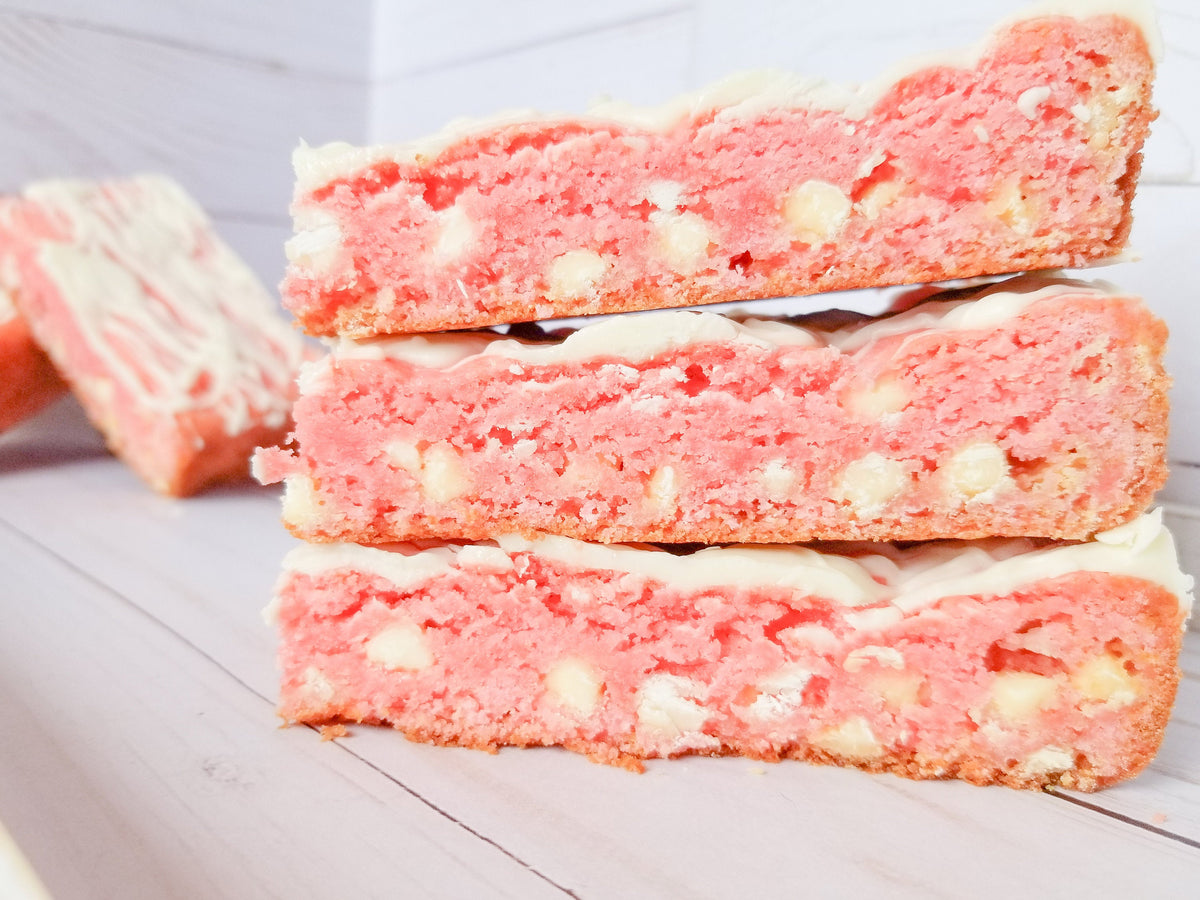 Strawberry blondies from Let's Get Baked Artisan Desserts, featuring layered cake bars with strawberry flavors and a golden finish.