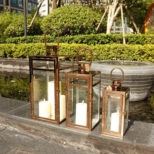 Set of 3 JHY DESIGN rose gold stainless steel outdoor decorative candle lanterns in 12, 15, and 19-inch sizes.