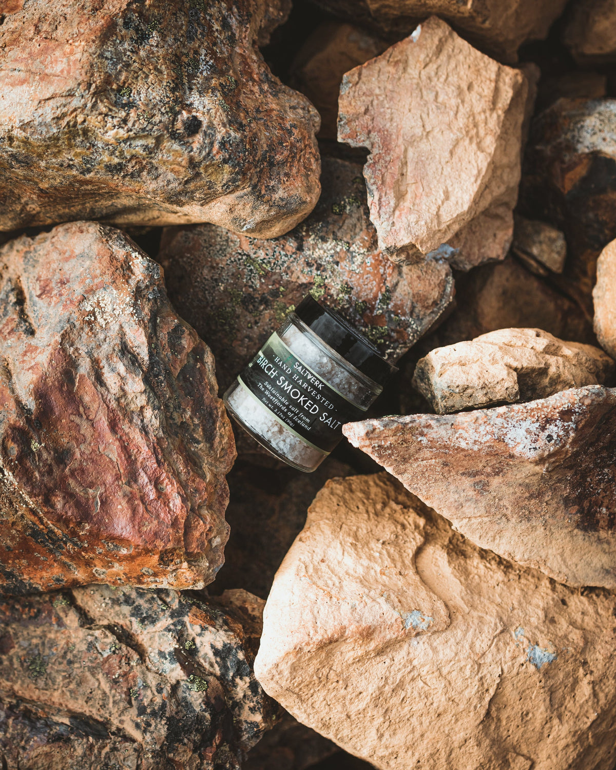 Jar of Saltverk Birch Smoked Salt with brown rocks, showcasing natural smoked salt in a clear glass jar.