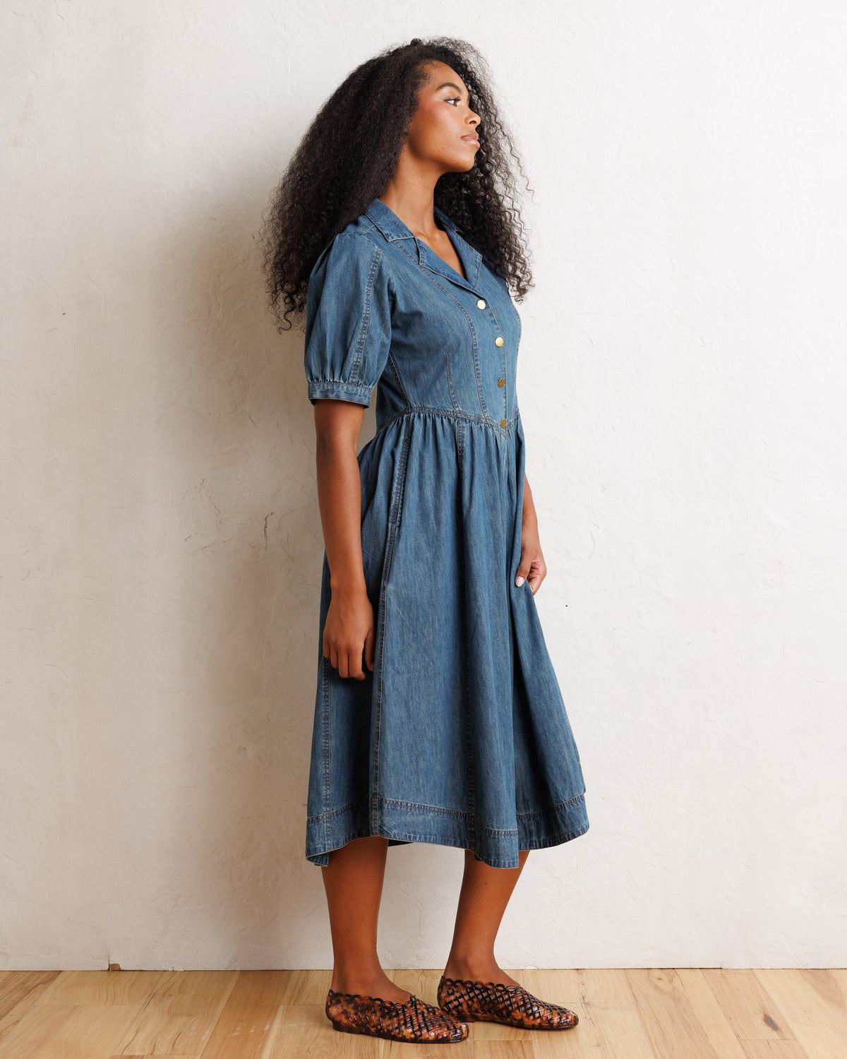 Downeast Orchard Denim Dress hanging on a wooden hanger, showcasing casual sleeveless dress with front pockets and button details.