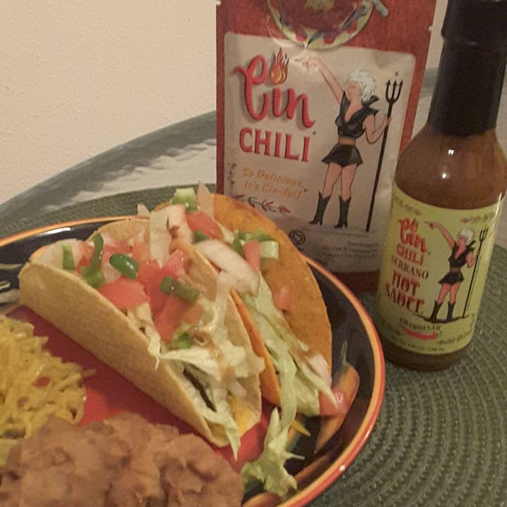 Bottle of Cinderosa Ranch Cin Chili Serrano Hot Sauce showing the label and vibrant orange-red sauce inside the clear glass bottle.