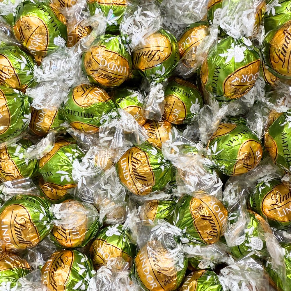 Assorted Lindt LINDOR Matcha White Chocolate Truffles in a bulk Candy In Bulk package, showing smooth white chocolate exterior