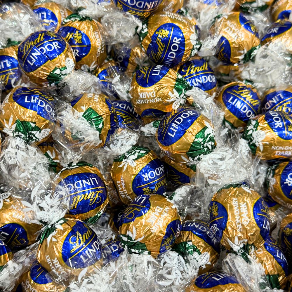 Two Lindt LINDOR Non-Dairy Oatmilk Dark Chocolate Truffles in a bulk Candy In Bulk bag, showcasing smooth, dark chocolate with a glossy finish.