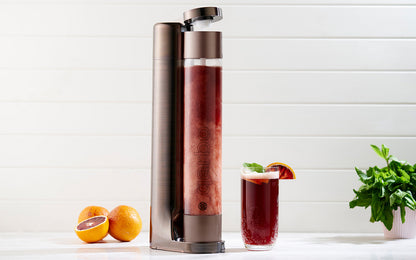 Qarbo FizzMaster sparkling water and fruit infuser in bronze by BACKUPMYFILESNOW®, with glass and fresh fruits for infusion.