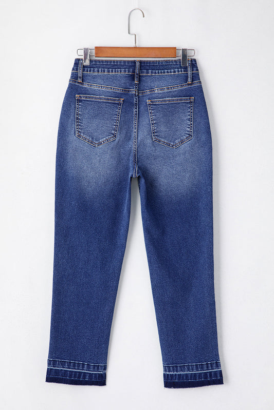 Light blue Jada Hem Cropped Jeans by Threaded Pear displayed on a hanger with a casual urban background.