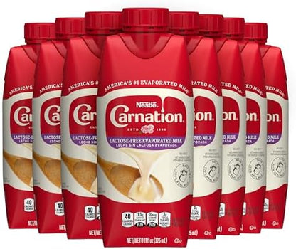 Eight cans of Carnation lactose-free evaporated milk stacked together, showcasing the product packaging and brand label.
