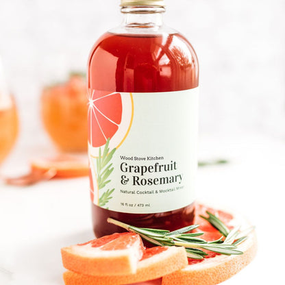 Wood Stove Kitchen grapefruit and rosemary cocktail and mocktail mixer in a 16 fl oz bottle, with fresh grapefruit and rosemary on the label.