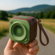 Compact portable wireless speaker with durable casing and wrist strap in outdoor setting