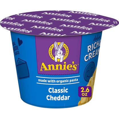 Annie's Homegrown White Cheddar Mac & Cheese microwavable cups, 8-pack, showing creamy cheese sauce and pasta in a cup.