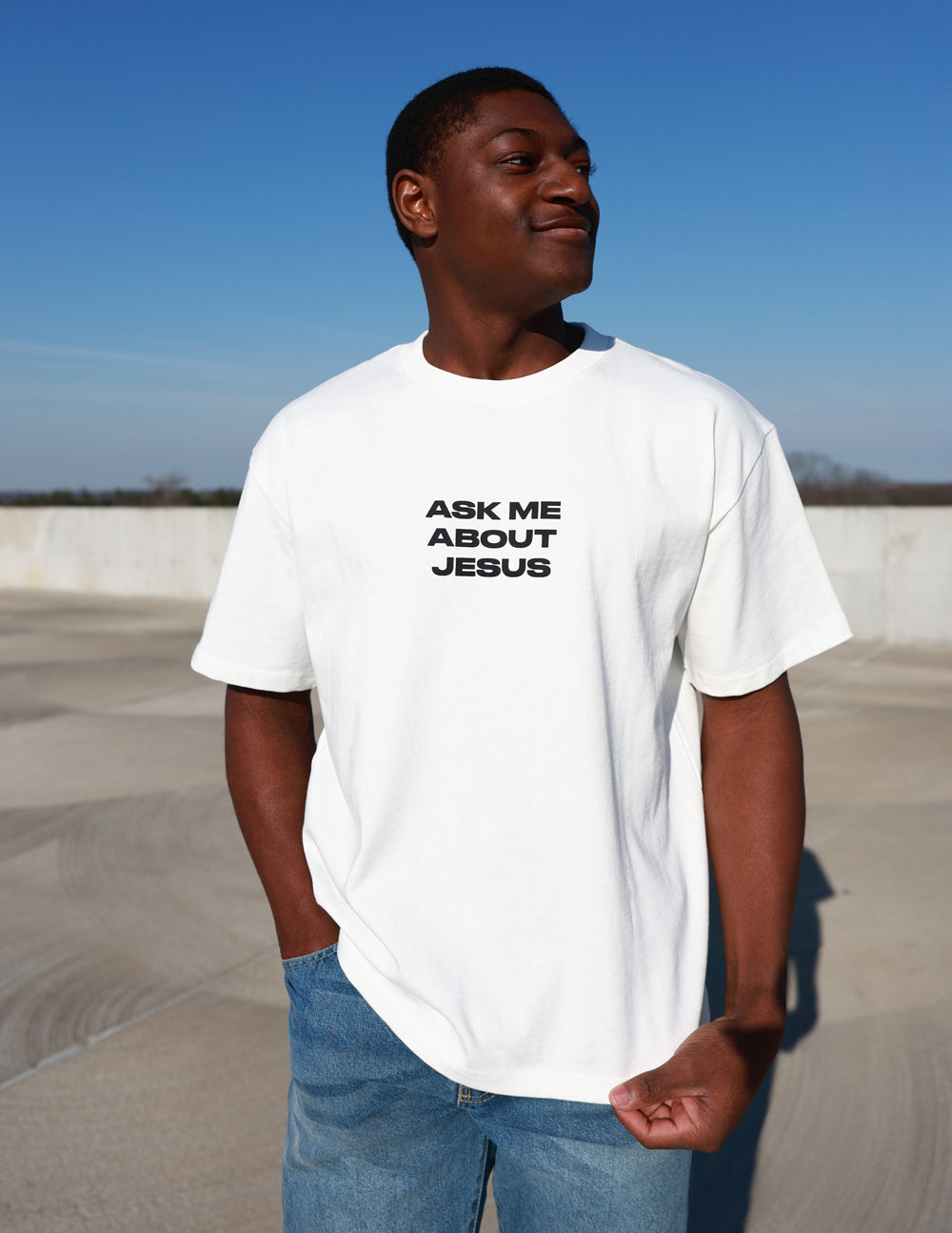 Black heavyweight T-shirt by Elevated Faith featuring bold "Ask Me About Jesus" graphic on front.