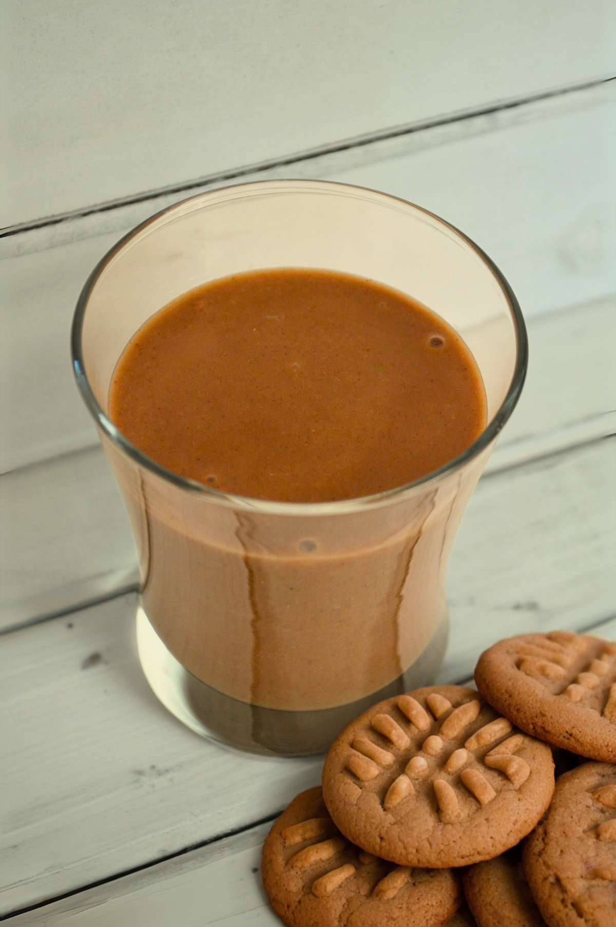 Creamy chocolate peanut butter shake by AmBari Nutrition in a glass, topped with whipped cream and sprinkled with cocoa powder.