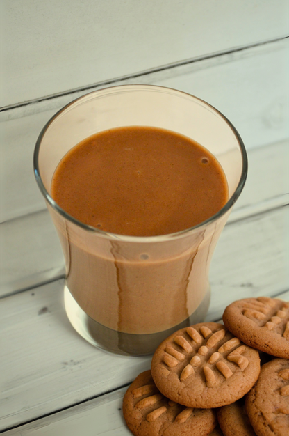Creamy chocolate peanut butter shake by AmBari Nutrition in a glass, topped with whipped cream and sprinkled with cocoa powder.