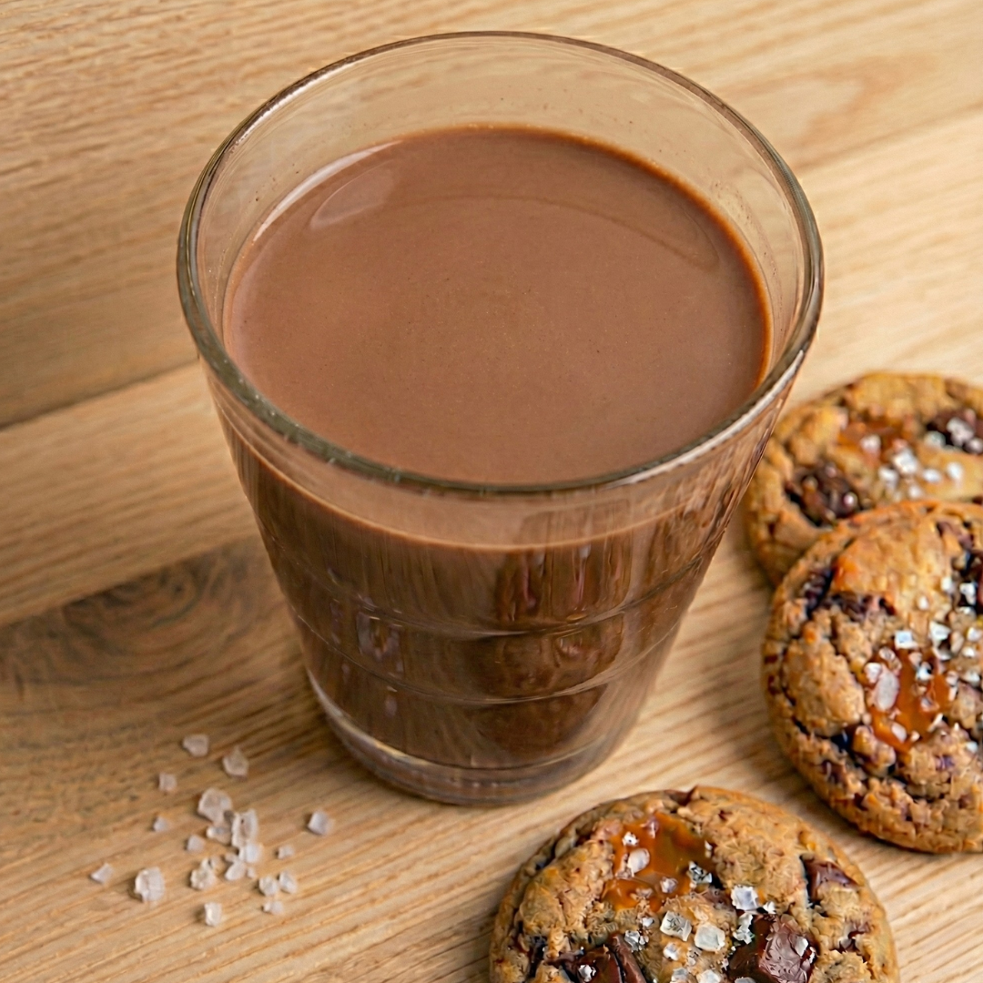 Chocolate salted caramel protein shake by AmBari Nutrition in a clear glass topped with caramel drizzle and chocolate syrup.