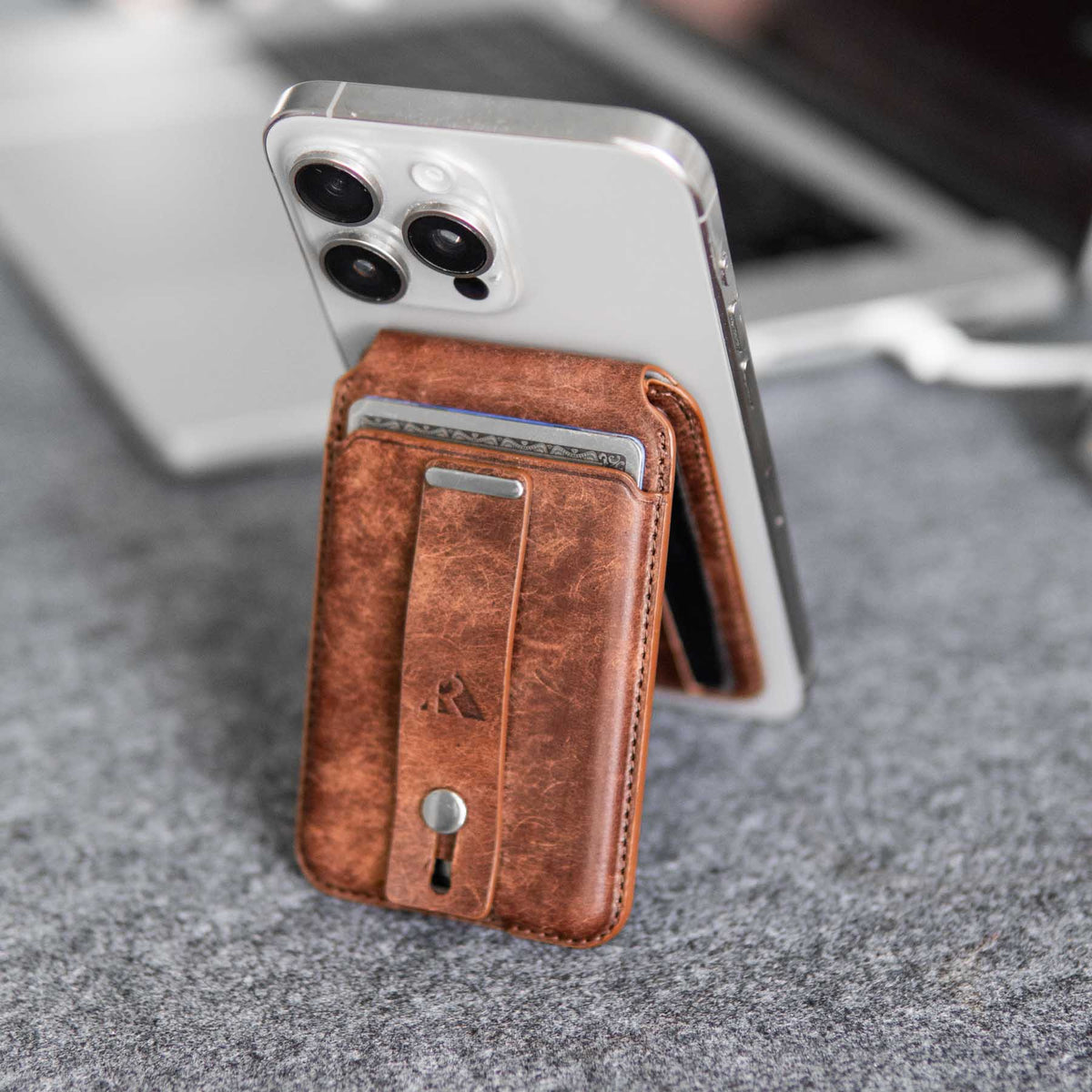 Magnetic cardholder in brown leather with card slots, attached to a smartphone, on a gray surface.