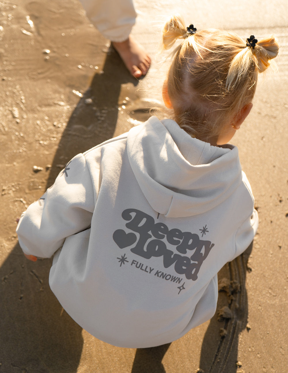 Pink kids hoodie with "Deeply Loved" text from Elevated Faith, featuring a cozy hoodie with a front pocket and soft fabric.