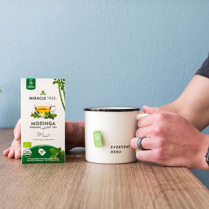 Organic Moringa Tea with fresh mint leaves by Miracle Tree, caffeine-free herbal tea in a clear glass cup.