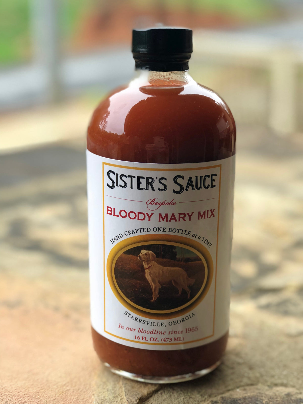 Bottle of Sister's Sauce Bloody Mary Mix with label visible, showcasing the beverage's spicy, flavorful tomato-based drink in a clear glass.