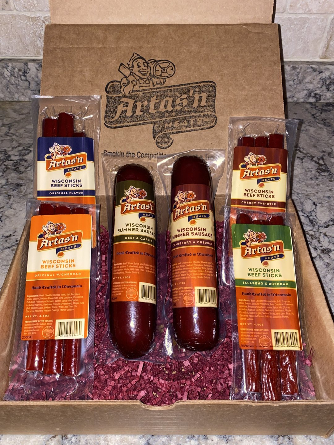 Artas'n Meats Wisconsin Six Pak gift box with assorted sausage sticks arranged inside.