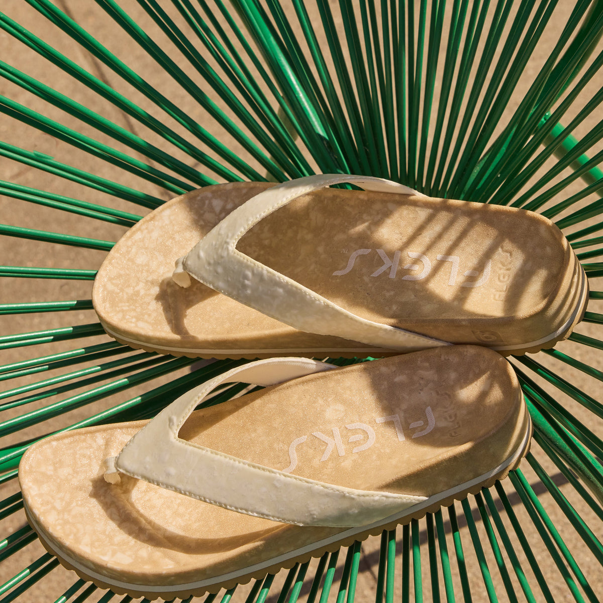 Fleks West Beach Flip Flop in oatmeal color, showing the casual slip-on design and textured sole on a sandy beach setting.