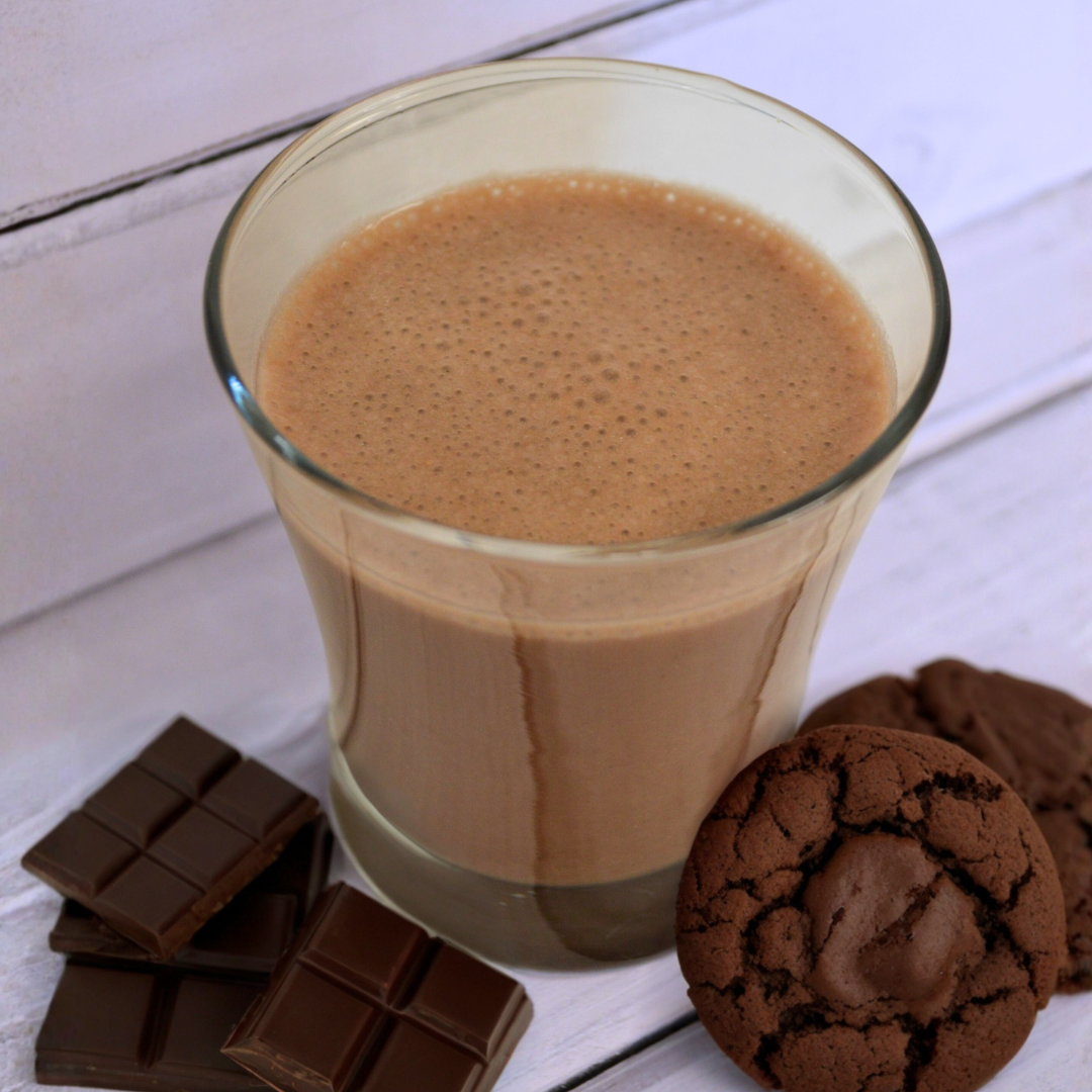 Creamy milk chocolate shake from AmBari Nutrition in a glass with a straw, topped with whipped cream and chocolate drizzle.