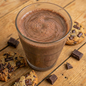 Creamy milk chocolate shake from AmBari Nutrition in a glass, topped with whipped cream and chocolate drizzle.