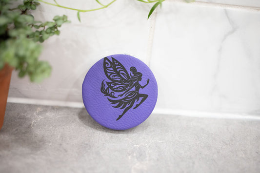 Double-sided compact mirror with faux leather cover from The McGarvey Workshop, showing reflective surfaces and textured exterior.