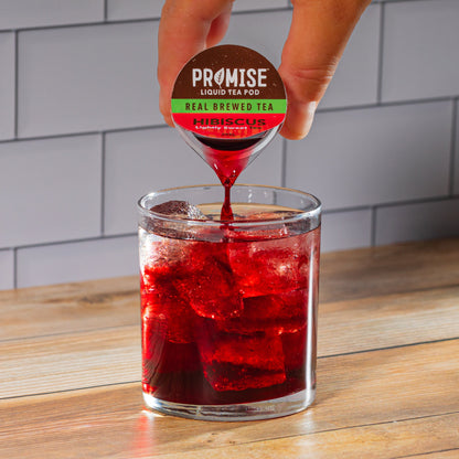 Java House Promise Real Brewed Hibiscus Tea in a clear glass bottle with vibrant hibiscus flowers and deep red tea inside.