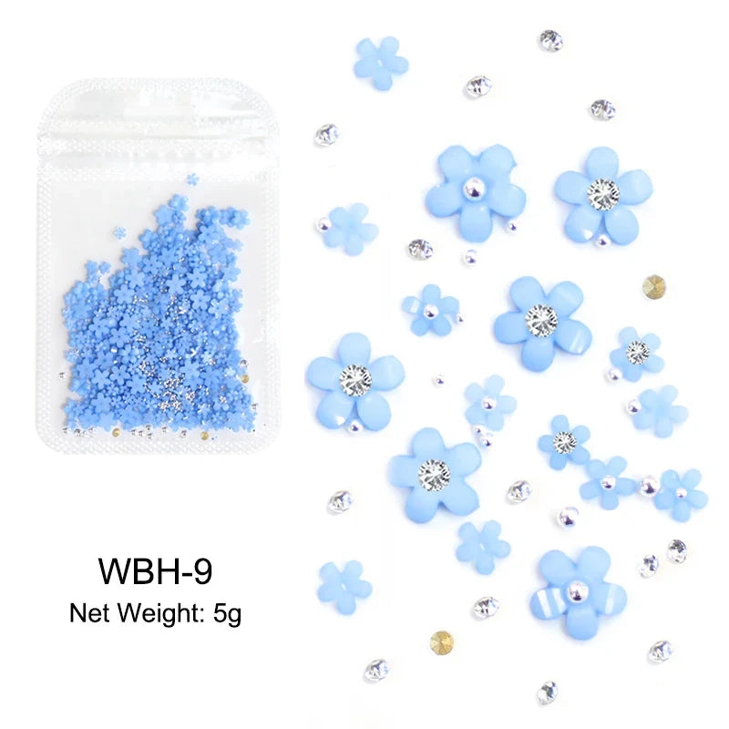 White acrylic flower nail art decorations with mixed size rhinestones and red-blue gems for DIY manicure design.