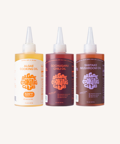 Algae Cooking Club Chef Squeeze Trio oil bottles with colorful labels, arranged on a white surface.