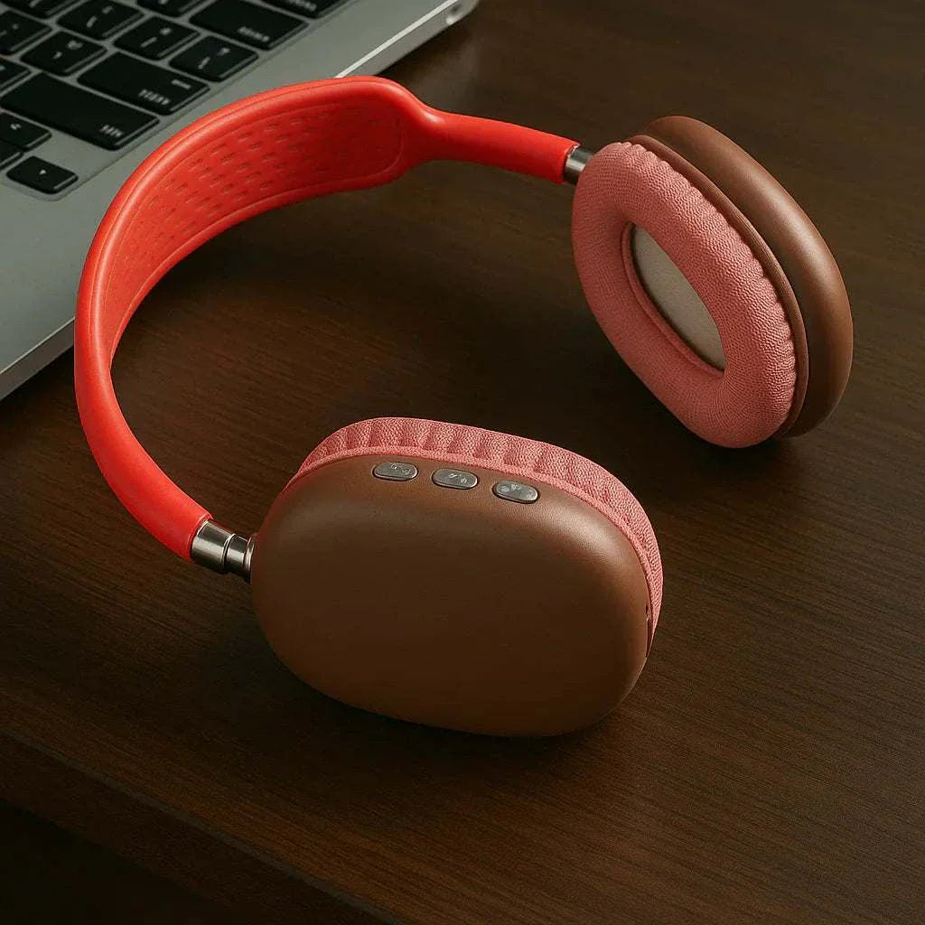 Wireless Bluetooth headphones in brown and red with cushioned ear pads on a wooden desk next to a laptop keyboard