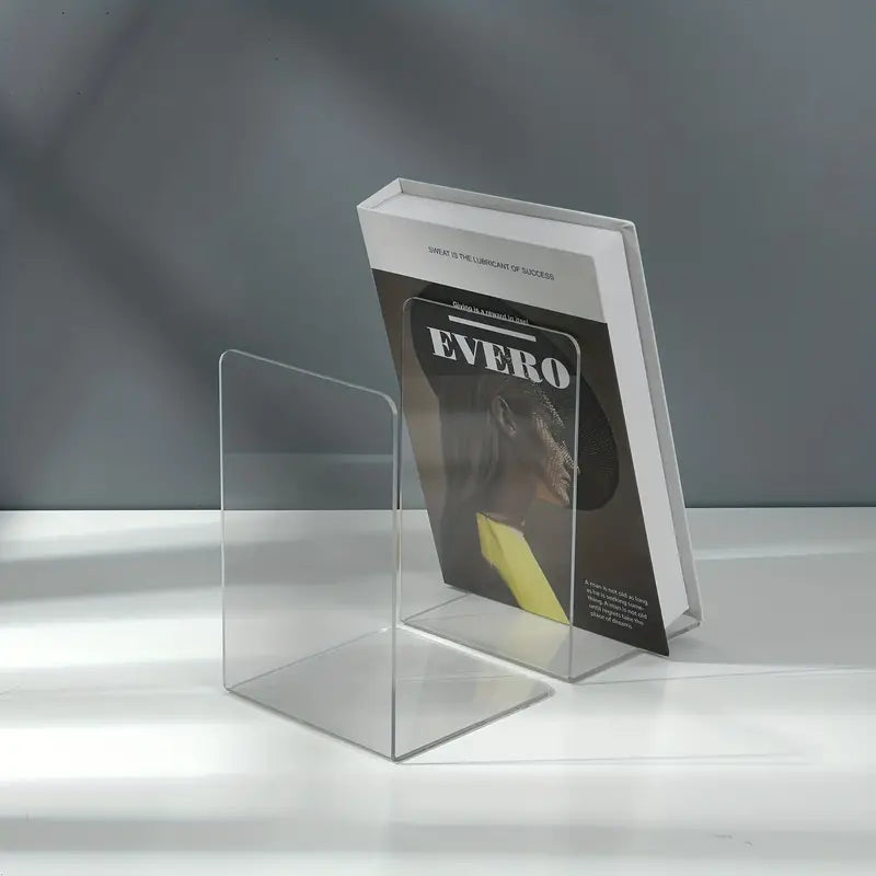 Clear acrylic desktop book stand from BACKUPMYFILESNOW.COM® holding an open book on a workspace.