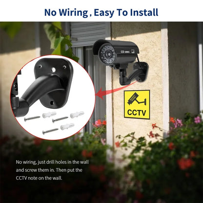Black dummy security camera with red flashing LED light, battery-powered, suitable for indoor and outdoor security deterrence.