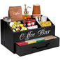 Black wooden coffee station organizer with compartments for cups, coffee pods, sugar, and accessories on a countertop.