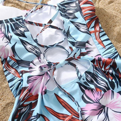 Family matching swimwear with floral pattern for kids and adults, including ruffle one-piece swimsuit and swim shorts at the beach.