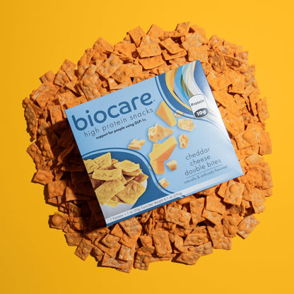 Biocare High Protein Cheddar Cheese Double Bites snacks with crispy cheese bites in a clear bowl on a wooden surface.