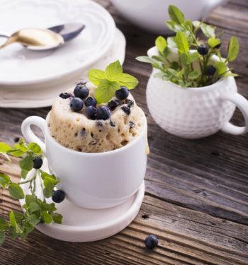 Blueberry Mug Cake by AmBari Nutrition in a bowl, showing a moist blueberry dessert with fresh blueberries on top.