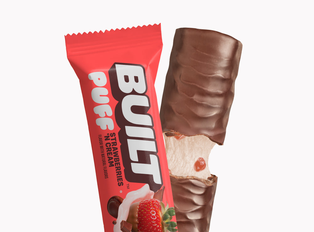 BUILT Strawberries 'N Cream Puff bar showing a creamy filling with fresh strawberry pieces on a textured surface.