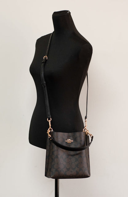 Coach Mollie 22 small bucket crossbody handbag in brown and black coated canvas with adjustable strap and signature design.