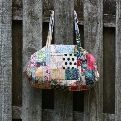 Patchwork quilted duffle bag from Darn Good Yarn with colorful fabric patches and sturdy handles.