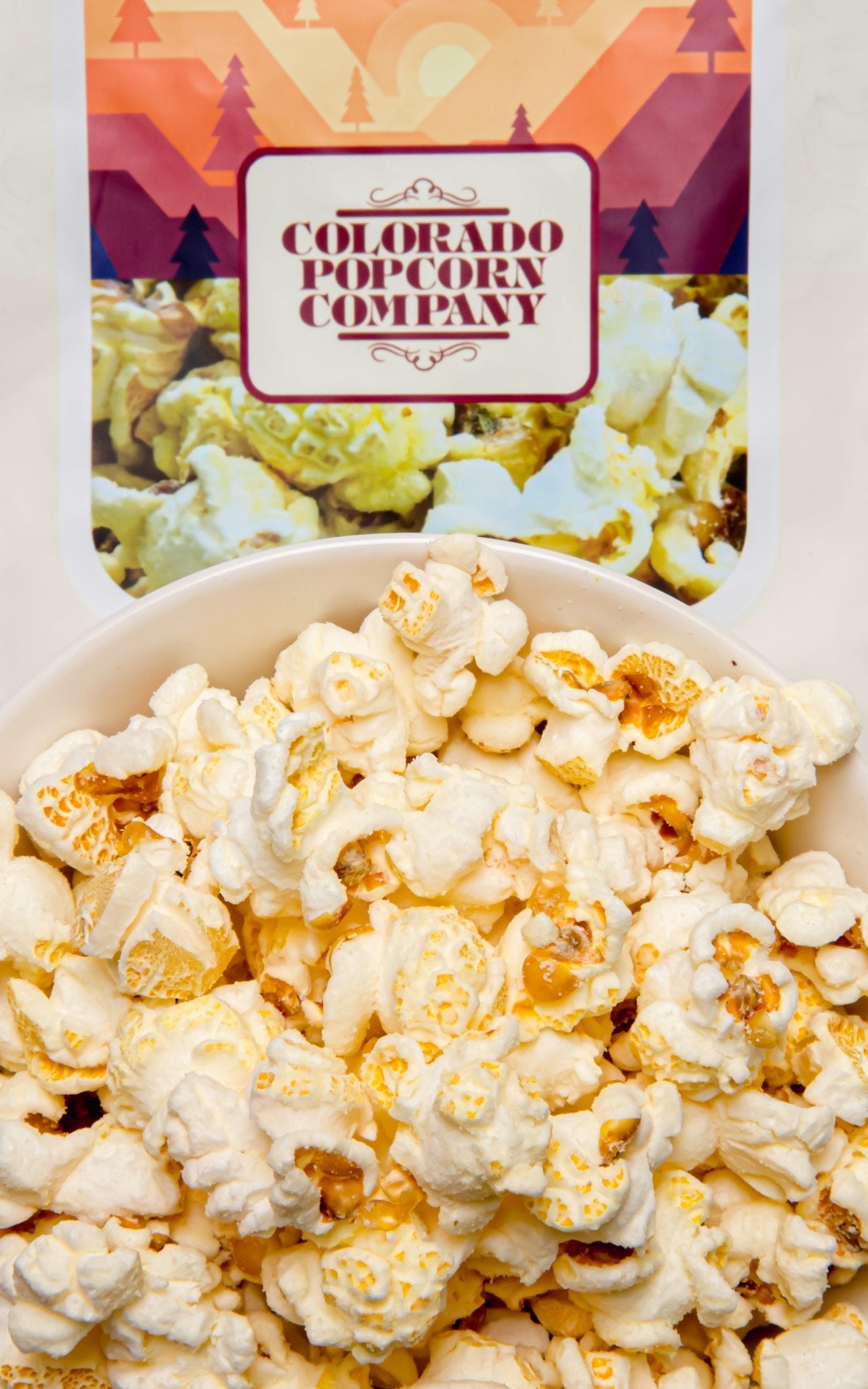 White cheddar popcorn in a clear bag from Colorado Popcorn Company, showing fluffy popcorn coated with white cheddar flavor.